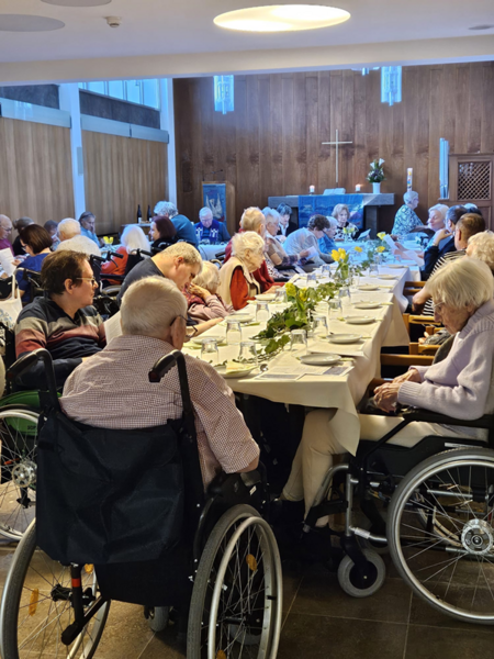 Beim Gründonnerstag-Gottesdienst im Hufeland-Haus sitzen Bewohner*innen und Angehörige zur Erinnerung an das letzte Abendmahl Jesu an schön geschmückten Tischen