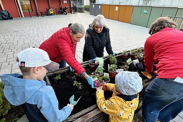 Kinder, Erwachsene und ältere Menschen beim Pflanzen in ein Hochbeet vor dem Hufeland-Haus.